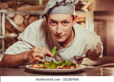 young male cook preparing delicious appetizer with herbs on white plate