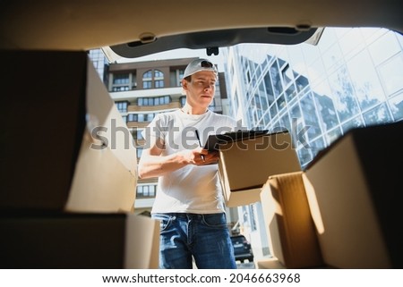 Young male courier with parcels near delivery service car