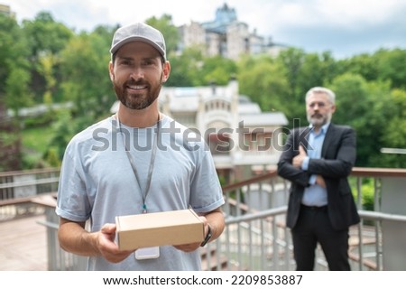 Young male courrier giving the box to the mature businessman