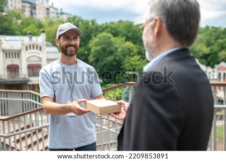 Young male courrier giving the box to the mature businessman