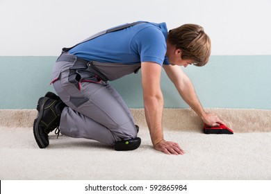 Young Male Craftsman Fitting Carpet On Floor