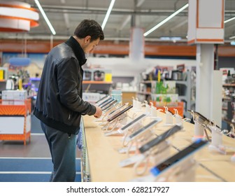 Young Male Customer Choosing Smartphone In The Mobile Phone Shop. Difficult Decision