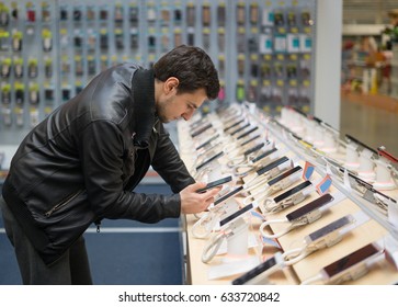 Young Male Customer Choosing Smartphone In The Mobile Phone Shop. Difficult Decision