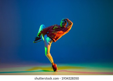 Young male dancer dancing hip-hop isolated over blue background in neon light