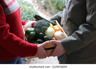 Young Male Delivering A Community Supported Agriculture (CSA) Fresh Produce Box To A Middle Aged Woman