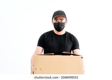 Young Male Delivery Man, Wearing Health Mask, Glasses, Protecting It From Pandemic, Dressed In Black, With Cap, Holding A Box, On White Background, Latino.