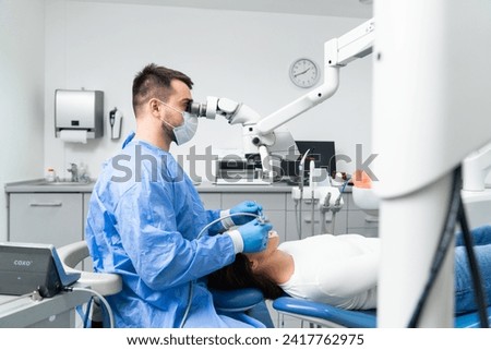 Young male dentist is examining the patient's teeth under a microscope in the dental office.