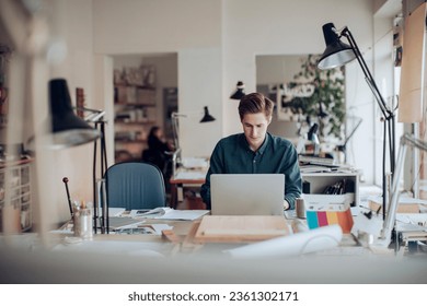 Young male designer using a laptop in a modern and contemporary business office - Powered by Shutterstock