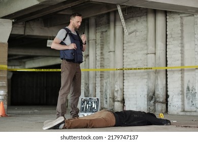 Joven investigador de detectives masculino o policía en chaleco antibalas de pie junto a cadáver mientras inspeccionaba la escena del crimen