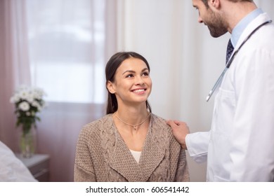 Young Male Doctor Consulting Smiling Female Patient In Hospital