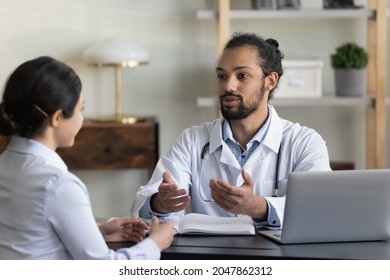 Young male doctor giving consultation, advice, recommendation to female patient, explaining, explaining treatment, checkup result at appointment, Indian woman consulting millennial practitioner
