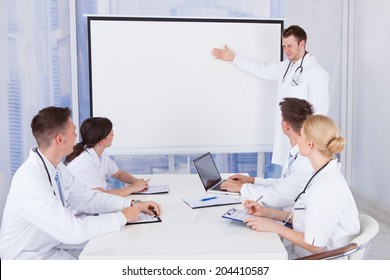 Young Male Doctor Giving Presentation To Colleagues In Conference Room