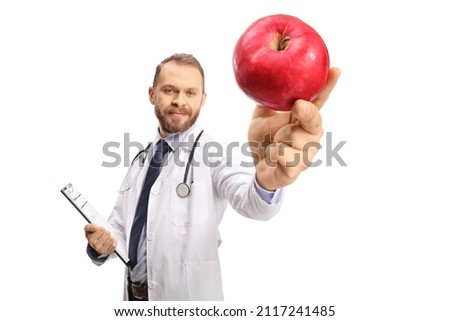 Young male doctor holding a clipboard and a red apple in front of camera isolated on white background 