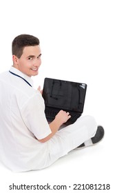 Young Male Doctor With A Laptop Sitting On A Floor With Legs Crossed And Looking Over Her Shoulder At Camera. Full Length Studio Shot Isolated On White.