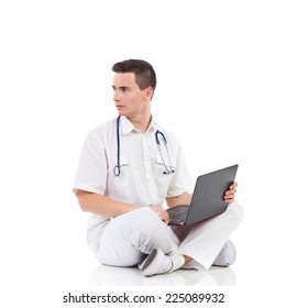 Young Male Doctor With A Laptop Sitting On A Floor With Legs Crossed And Back Over The Shoulder. Full Length Studio Shot Isolated On White.