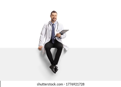 Young Male Doctor Sitting On A Blank Panel Isolated On White Background