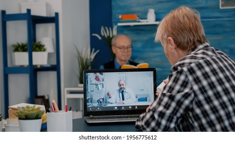 Young Male Doctor Talking To Senior Female Patient By Tele Medicine Online Video Call In Clinic. Physician Using Telehealth Medical Chat Virtual Healthcare Visit On Laptop Screen, Explaning Treatment