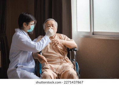 Young male doctor wearing lab coat with face shield mask and surgical mask for safety against covid-19 measuring temperature of senior old man sitting on wheelchair using thermometer in hospital room - Powered by Shutterstock