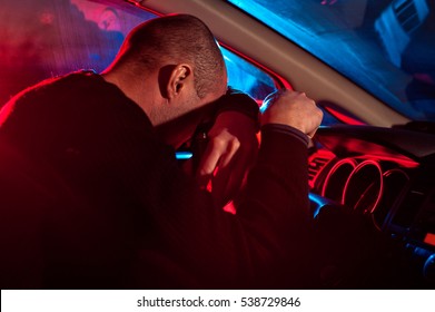 Young male driver is caught driving under alcohol influence. Man covering his face from police car light.