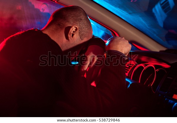 Young male driver is
caught driving under alcohol influence. Man covering his face from
police car light.