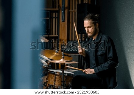 a young male drummer plays a drum kit in a recording studio at a professional musician's rehearsal recording song