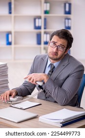 Young male employee and too much work at workplace - Shutterstock ID 2254499773