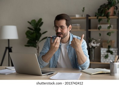 Young male employee sit at workplace desk holding smart phone talk to client on speaker phone, advanced user of modern tech, leaving voicemail, sending audio message, helps distantly by phone concept