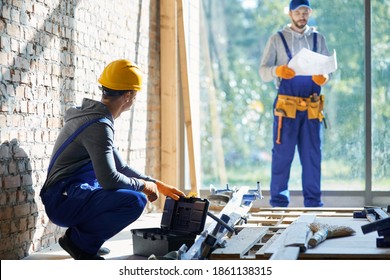 Young male engineer working at cottage construction site, picking instrument from toolbox with blurred colleague in the background on a sunny day