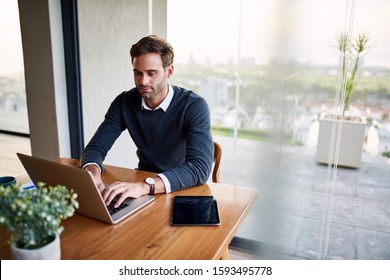 Young Male Entrepreneur Sitting At His Dining Room Table At Home Working Online With A Laptop