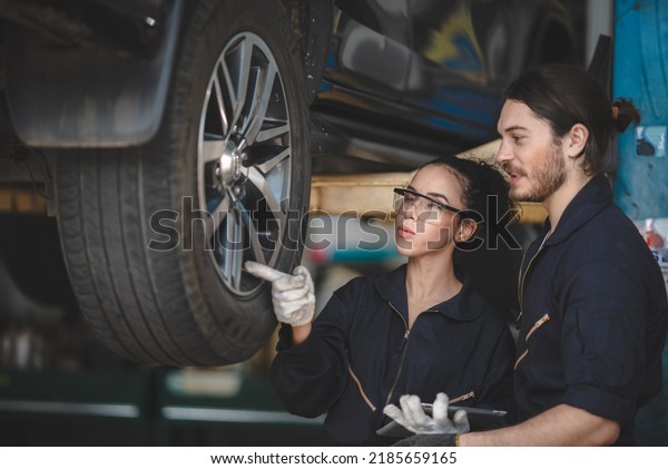 Young male and\
female car mechanic wearing uniform with safety eye glasses and\
hand gloves working on digital tablet while diagnosing problem in\
car in garage and\
discussing