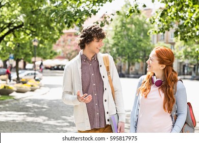 Young Male And Female College Students Talking While Walking On Footpath