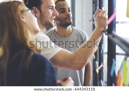 Young male and female coworkers writing remaining notes for colleagues planning productive working process in office, smiling students making memo stickers with to do list to organize daily schedule
