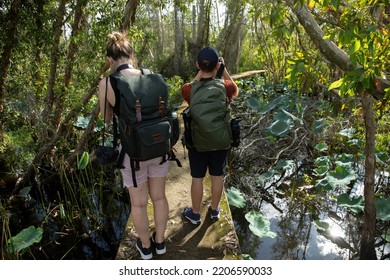 Young Male And Female Photographer From Back View Enjoying Hiking In A Tropical Forest Taking Photos Of Landscape.