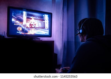 暗い部屋の中で、LEDテレビで見ているゲームコントローラを使って、眼鏡をかけた若い男性ゲーマーとヘッドセットを使ってビデオゲームをしている。ゲームとエンターテイメントのコンセプト