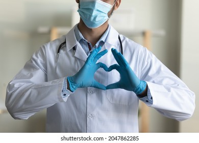 Young Male GP Doctor In Face Mask, Blue Protective Latex Gloves Showing Finger Heart Shape At Camera, Sending Love And Support To Medical Employees And Covid Patients. Epidemic, Medic Care Concept