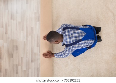 Young Male Handyman Rolling Carpet On Floor At Home