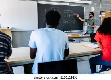 Young Male High School Tutor Standing In Front Of Blackboard Teaching Electronics Lesson To Multiracial Group Of Millennial Students - Teacher Explaining Technology Lecture In Classroom