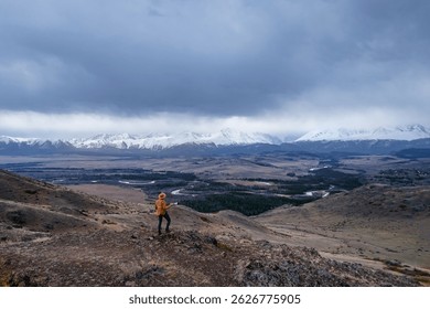 Young male hiker photographer with camera exploring rugged Altai mountains with snow-capped peaks under overcast sky. - Powered by Shutterstock - Get 15% off with code: PIKWIZARD15
