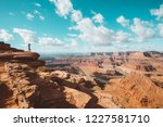 A young male hiker is standing on the edge of a cliff enjoying a dramatic overlook of the famous Colorado River and beautiful Canyonlands National Park in scenic Dead Horse Point State Park, Utah, USA