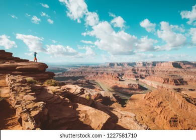 A young male hiker is standing on the edge of a cliff enjoying a dramatic overlook of the famous Colorado River and beautiful Canyonlands National Park in scenic Dead Horse Point State Park, Utah, USA - Powered by Shutterstock