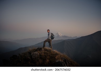 A young male hiker standing at the top of a grassy mountain and admiring the foggy nature