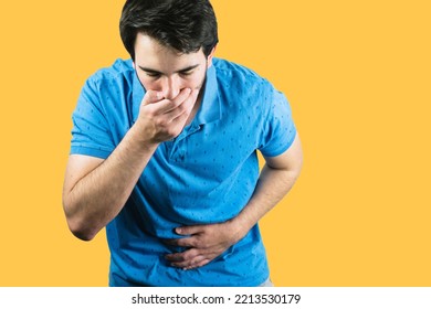 A Young Male Holding His Belly With One Hand And The Mouth With The Other Throwing Up From Food Poisoning With A Yellow Background