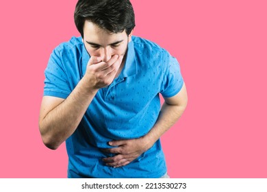 A Young Male Holding His Belly With One Hand And The Mouth With The Other Throwing Up From Food Poisoning With A Pink Background