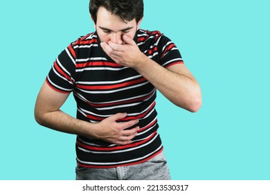 A Young Male Holding His Belly With One Hand And The Mouth With The Other Throwing Up From Food Poisoning With A Blue Background