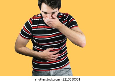 A Young Male Holding His Belly With One Hand And The Mouth With The Other Throwing Up From Food Poisoning With A Yellow Background