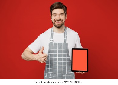 Young male housewife housekeeper chef cook baker man wear grey apron hold use digital tablet pc computer with blank screen workspace area isolated on plain red color background . Cooking food concept - Powered by Shutterstock