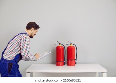 Young Male Inspector Taking Notes With A Pen While Checking The Condition Of Dry Chemical Or Carbon Dioxide Fire Extinguishers In The Building. Fire Safety, Fire Service, Fire Prevention Concepts