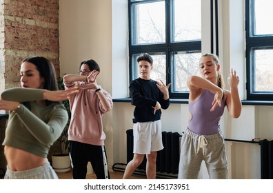 Young male instructor of vogue dancing group consulting teenage girls and guy in activewear repeating new movement at training