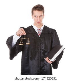 Young Male Judge Holding Golden Scales And Book Over White Background