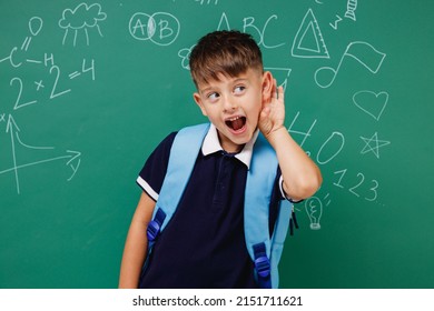 Young male kid school boy 5-6 years old in t-shirt backpack try hear you overhear listen intently isolated on green wall chalk blackboard background Childhood children kids education lifestyle concept